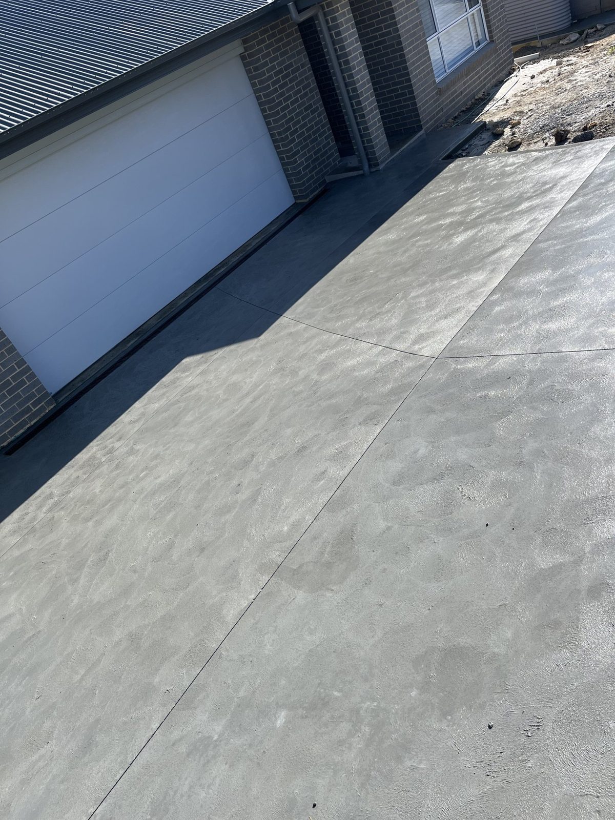 Plain concrete driveway leading to a garage by EAB Concreting, Hunter Valley